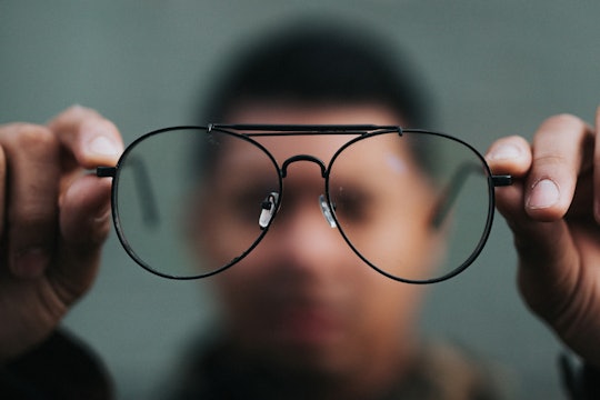 glasses blurry person in the background holding eyeglasses toward the camera