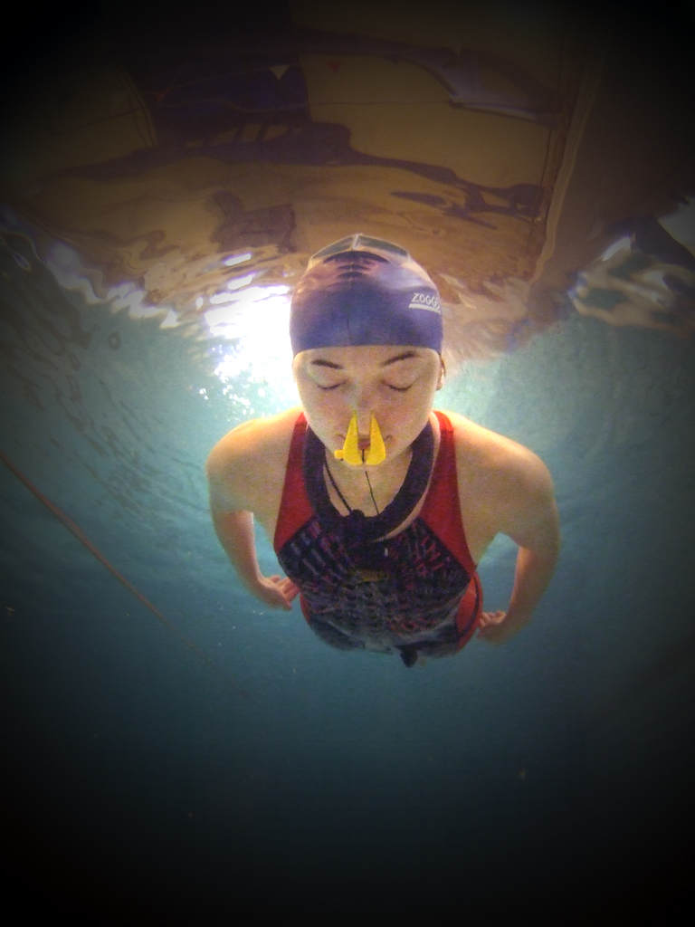 a person swimming in a pool wearing a swim cap and nose clip