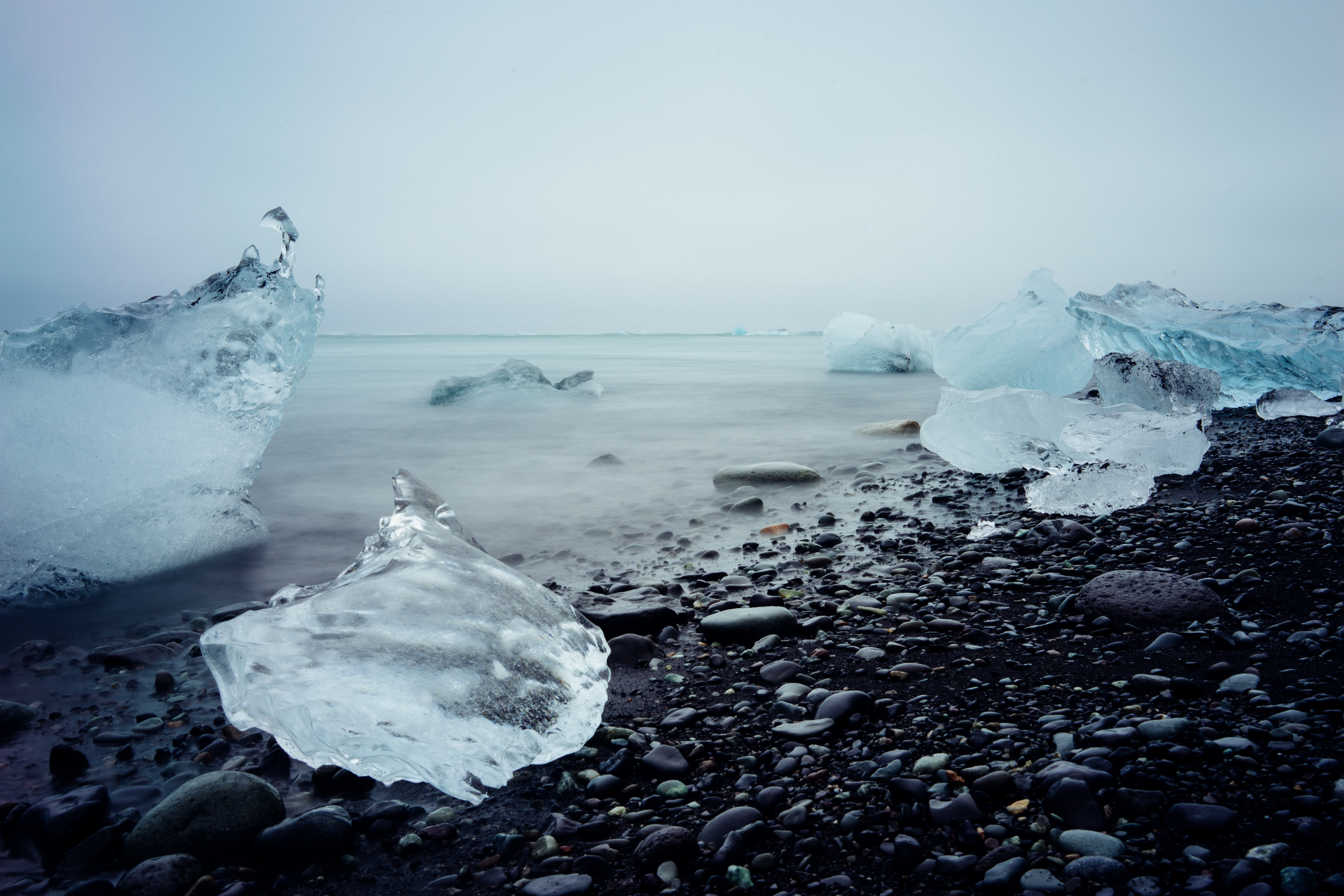 Melted sea ice seen from a shore of black stones.