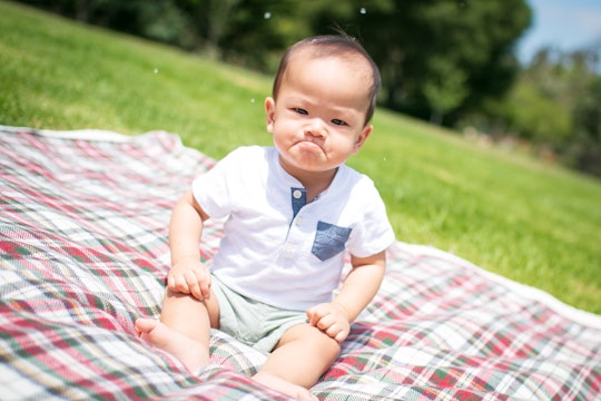 cute baby sitting on blanket outside making grumpy face