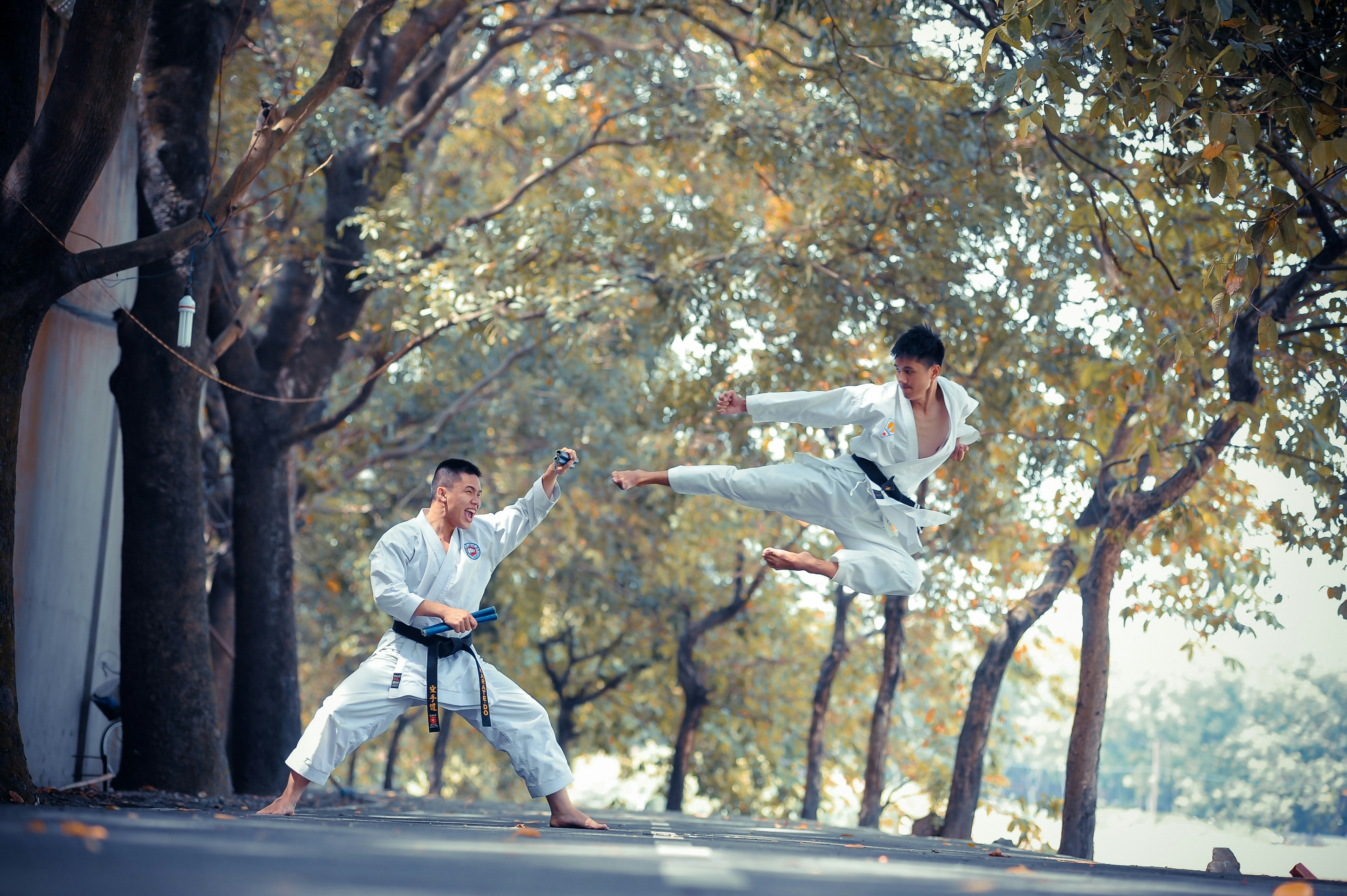 Two men performing martial arts. One is doing a flying kick towards the other.