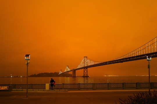 A couple looks out on the Golden Gate Bridge with an orange sky from California wildfires, September 2020
