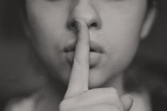A person holds a finger to mouth to shush someone.