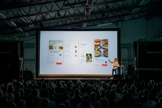 A man standing on stage presents at a conference in front of an audience.