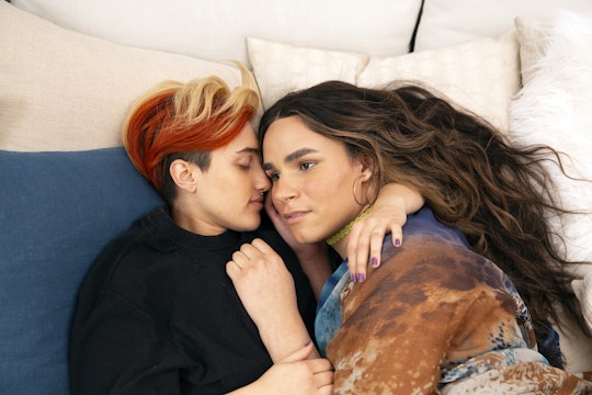A transmasculine gender-nonconforming person and transfeminine non-binary person waking up together in bed, cuddling.