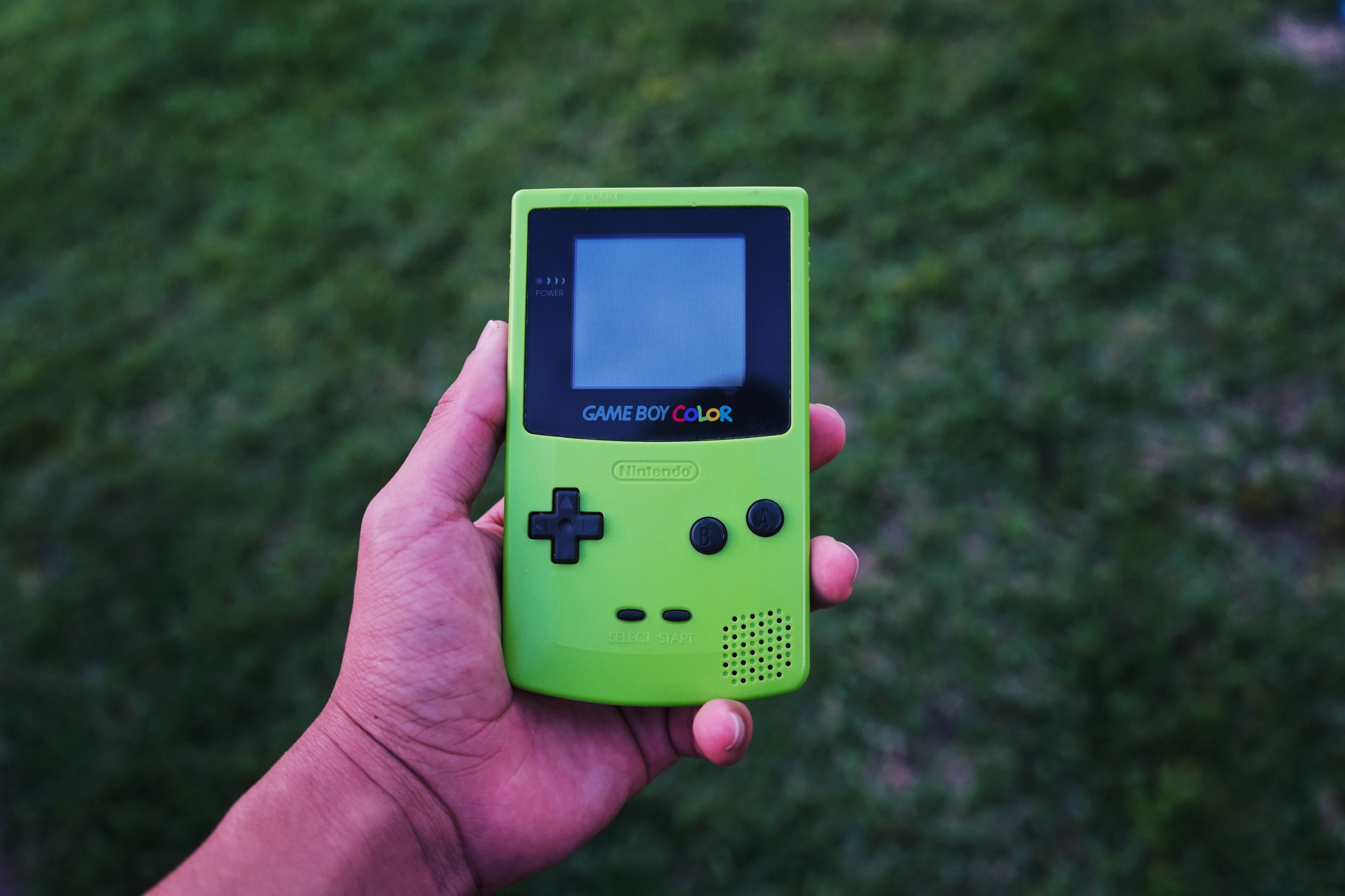 A person holding a green Game Boy Color in their hand