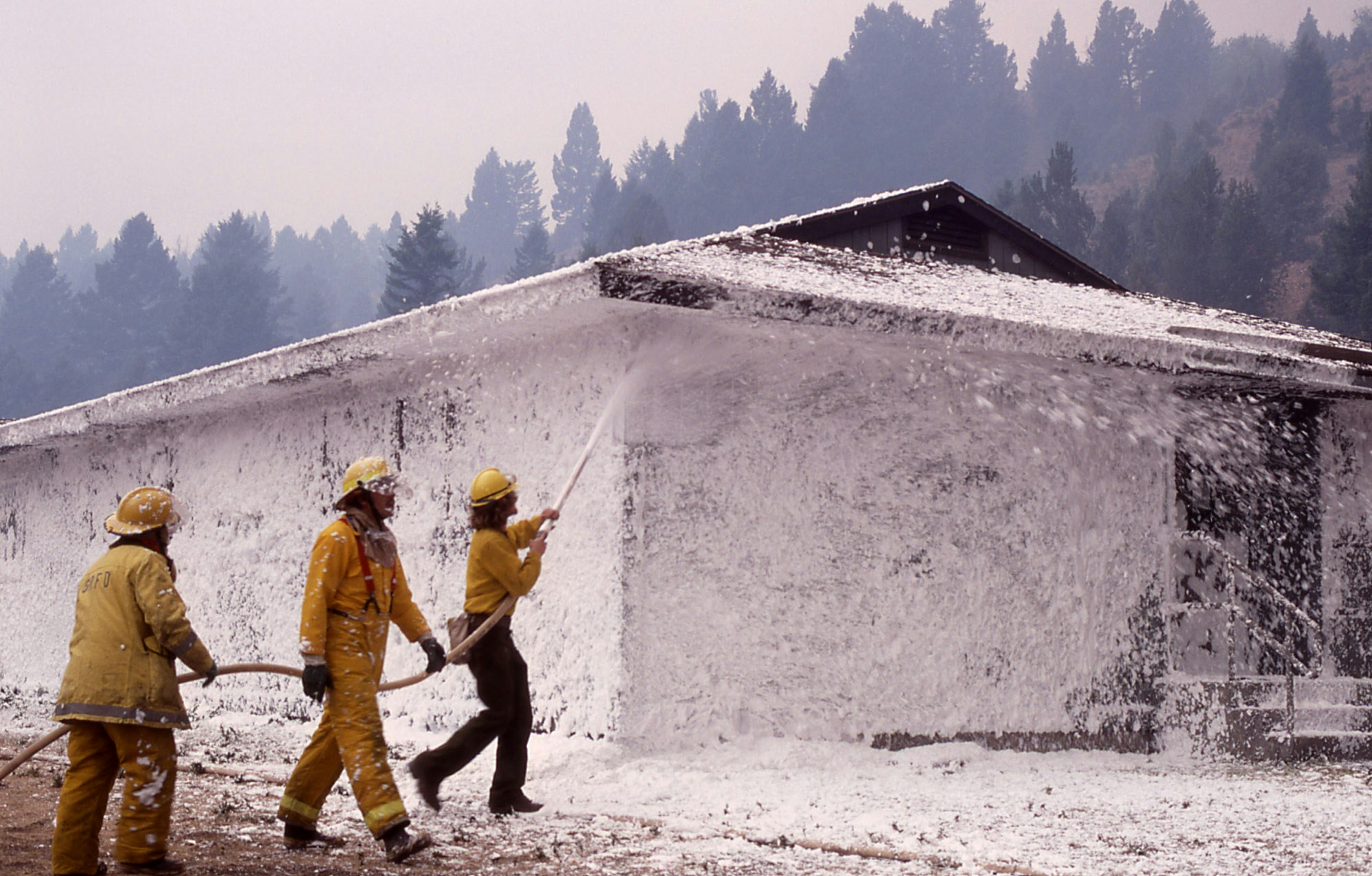 Three firefighters coat a small house in foam during a wildfire. 