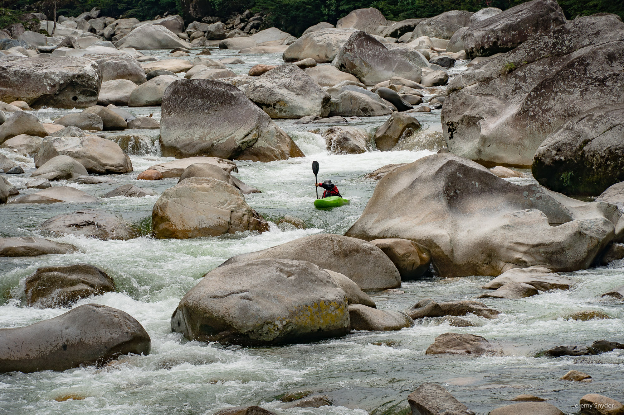 A kayaker paddles the Piatua river in Ecuador, among boulders brought down from the Andes