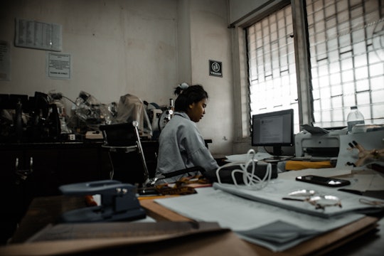 A scientist sitting a computer, surrounded by microscopes under plastic sleeves.