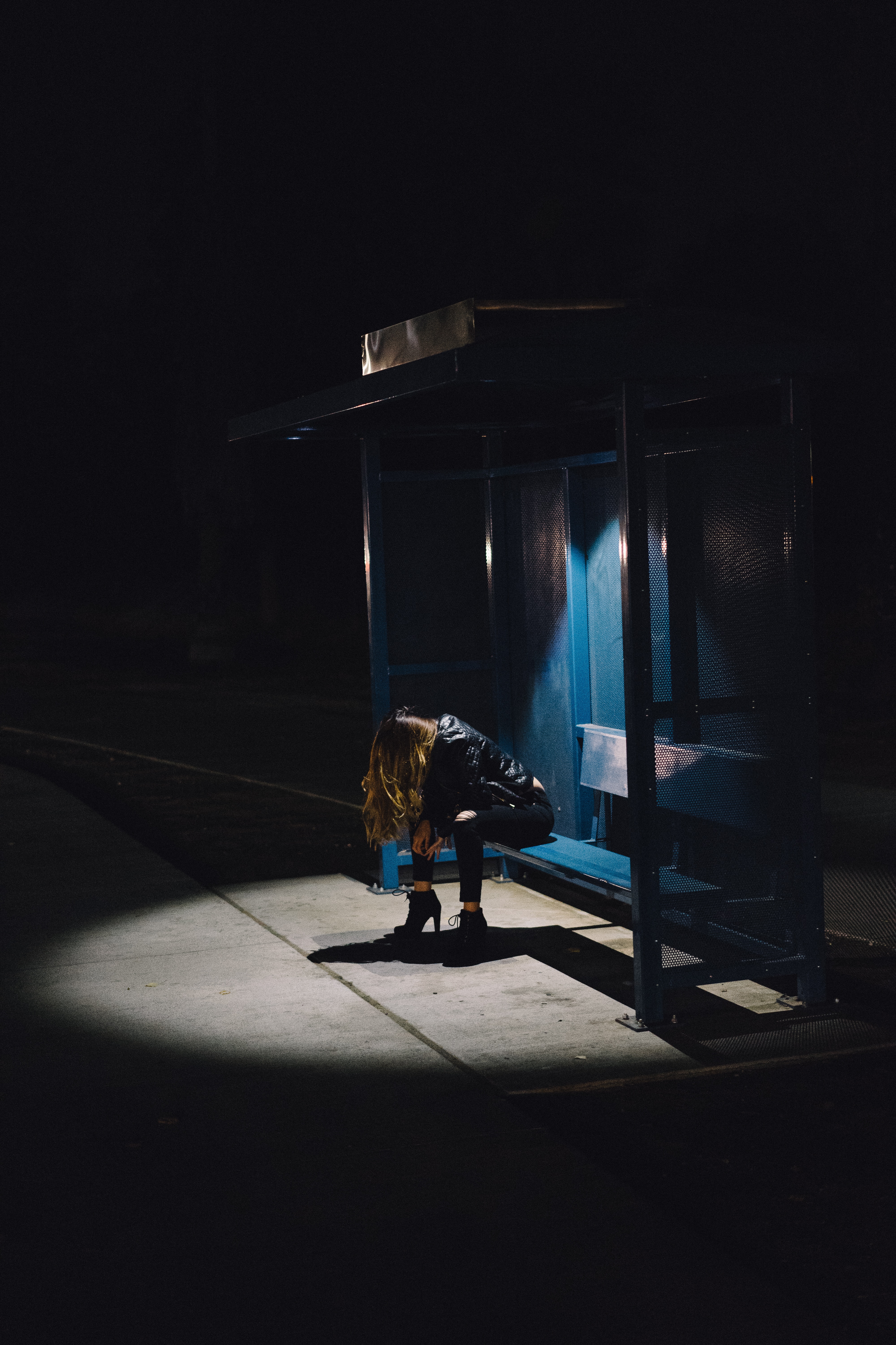 A woman sits at a bus stop with their head in their hands.