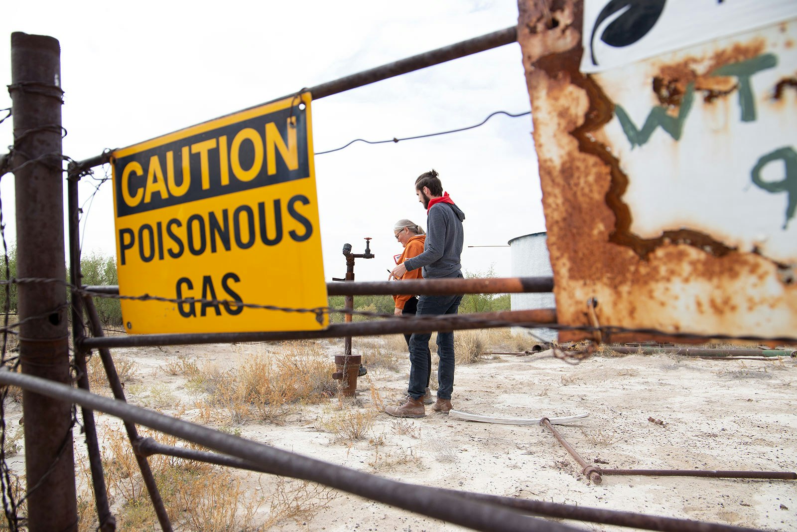 people standing behind a fence that has a sign that says "caution, poisonous gas"