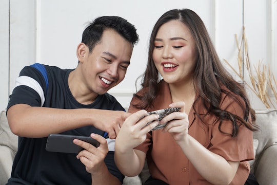 two people sitting on a sofa holding phones smiling laughing