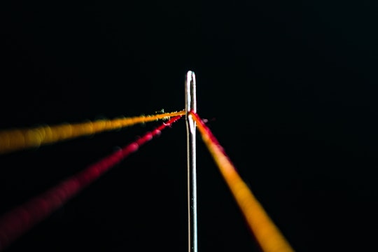 The head of a sewing needle with red and yellow thread threaded through it.