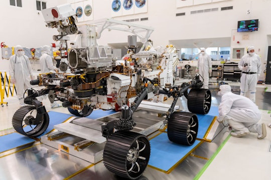 a mars rover being worked on in a lab by scientists in white clean suits