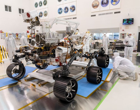 a mars rover being worked on in a lab by scientists in white clean suits