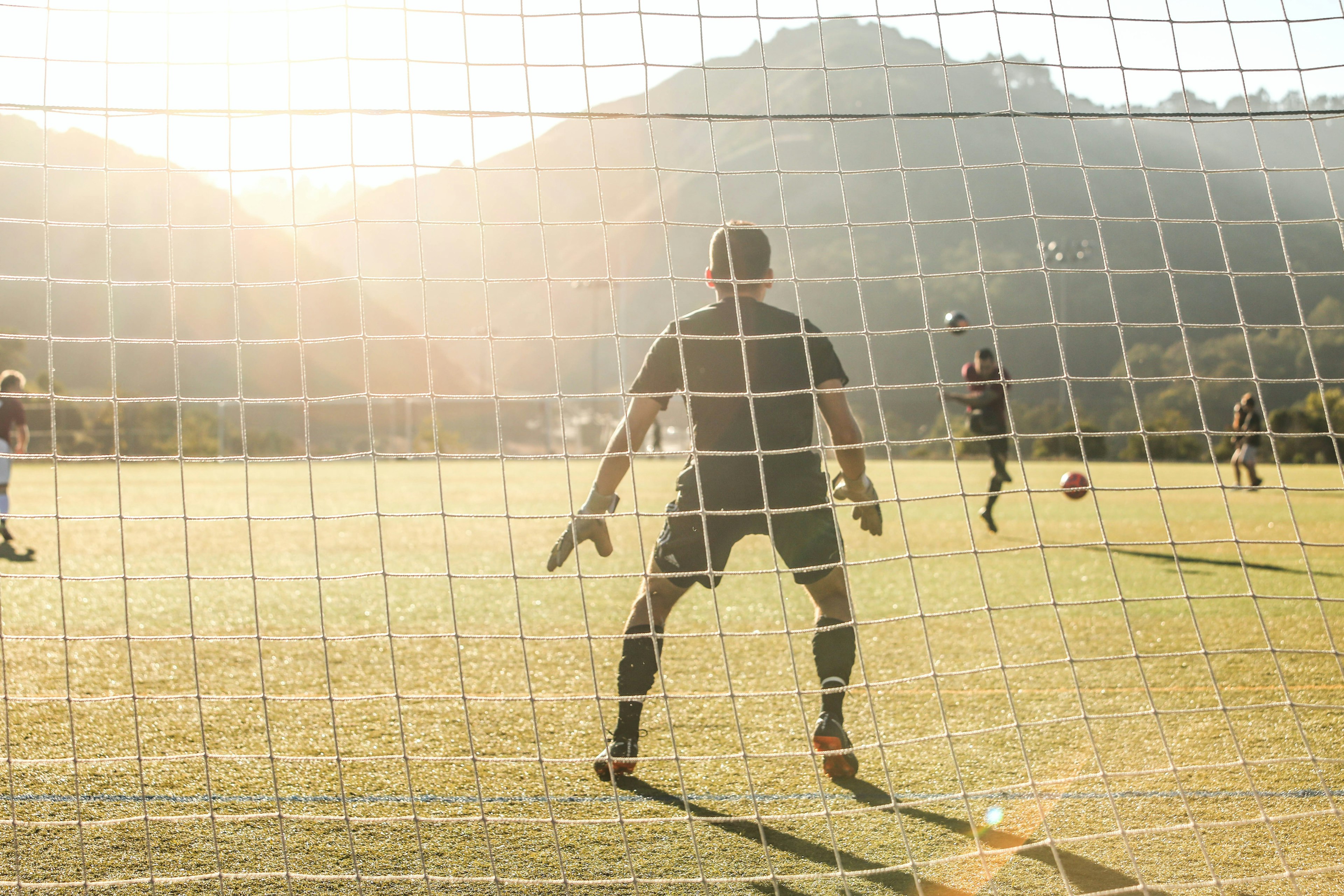 picture of a soccer goalie from behind the net during the daytime