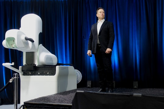 Elon Musk stands on stage next to a Neuralink device