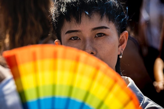A person looks out from behind a rainbow-colored fan.