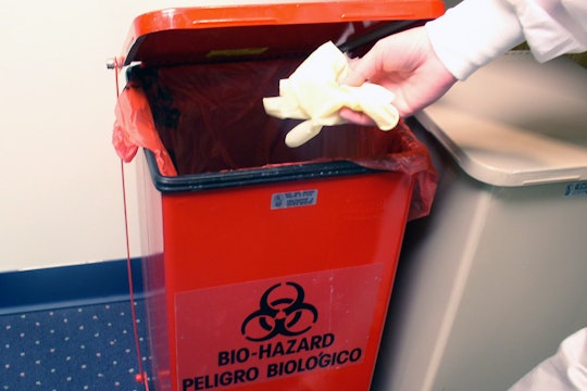 A plastic glove being thrown in hazardous waste garbage bin.