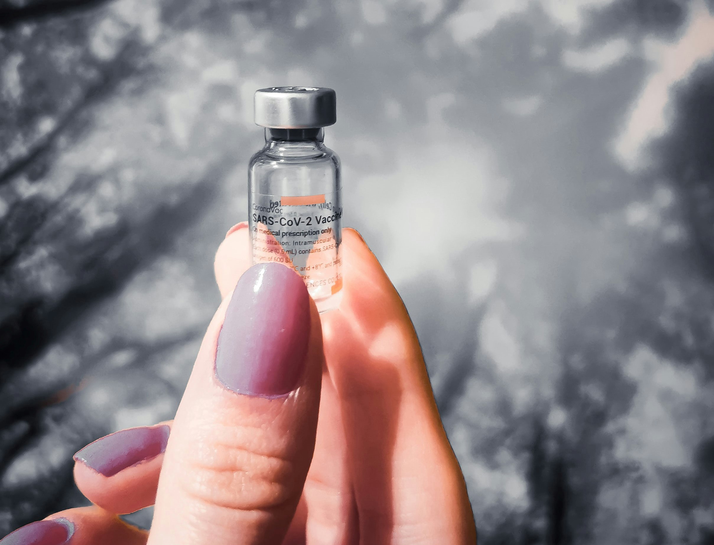 a woman's hand holding a vial of vaccine against a sky backdrop
