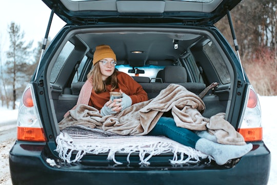 A woman sitting the trunk of a car drinking coffee, under a blanket