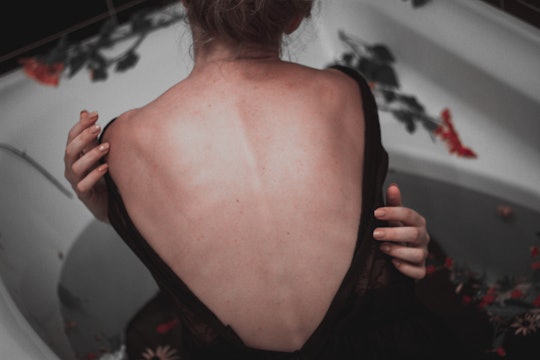 A woman grasping herself, with her back and spine exposed.