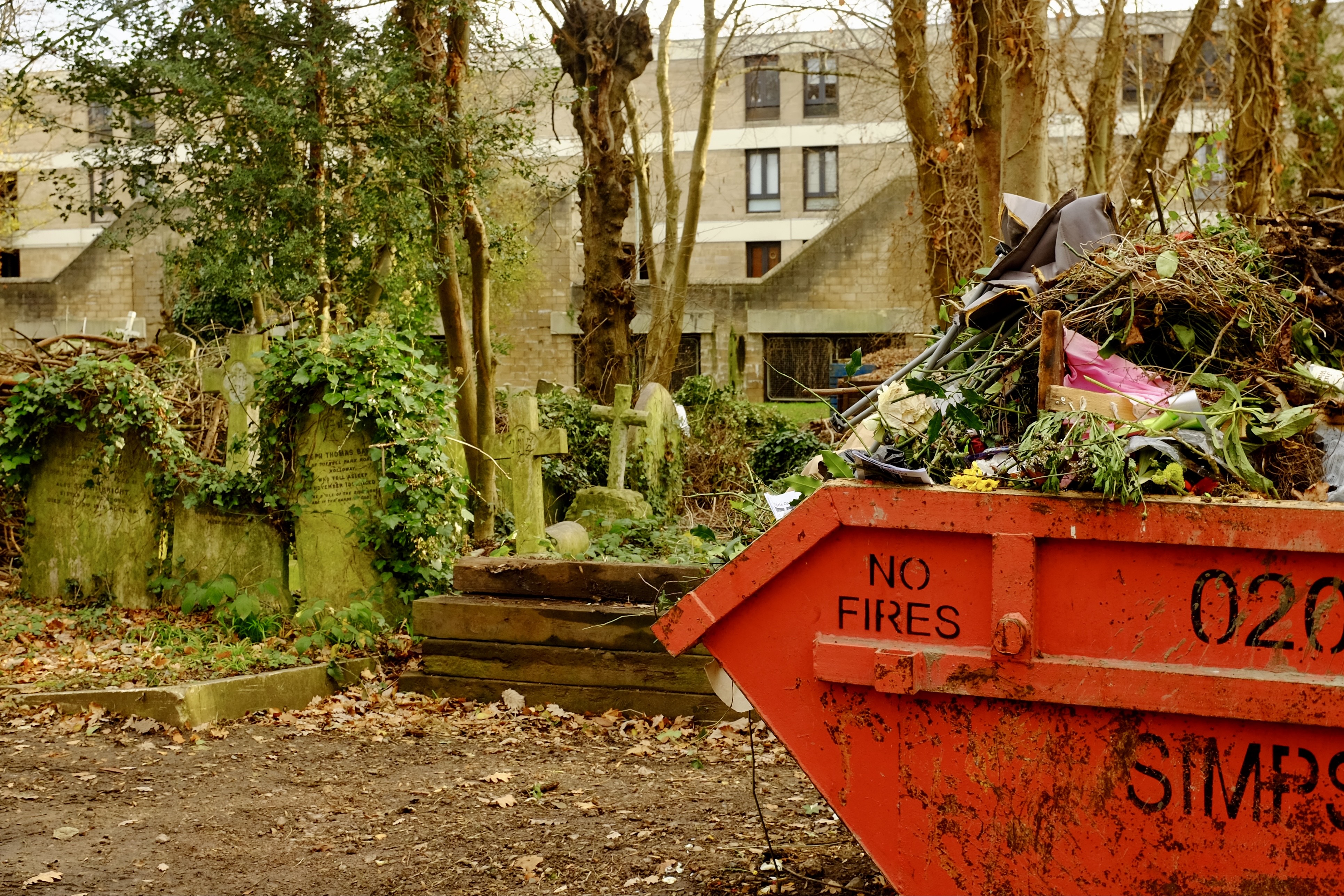 A large dumpster near a traditional cemetery 