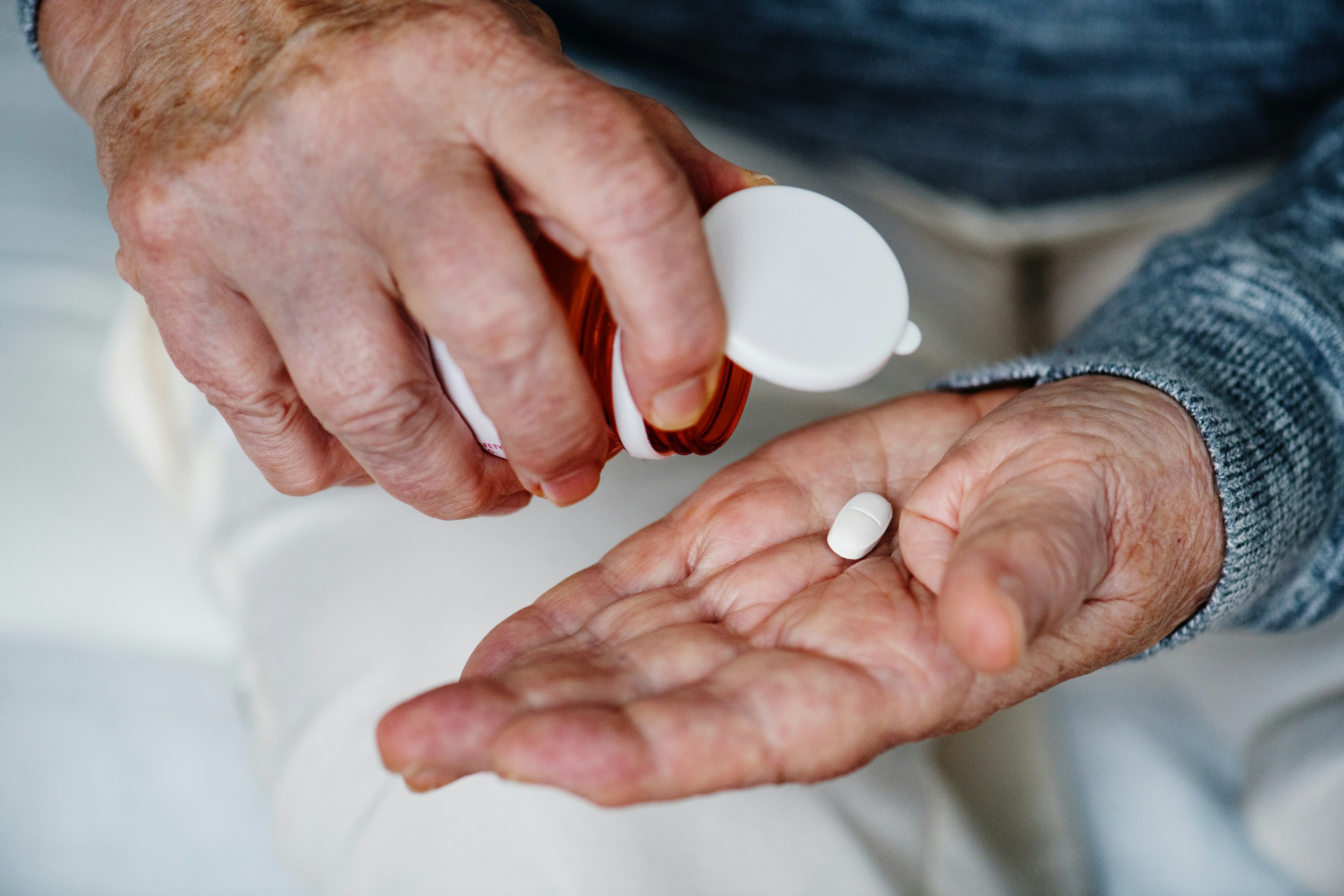 white hands holding one white, oval-shaped pill