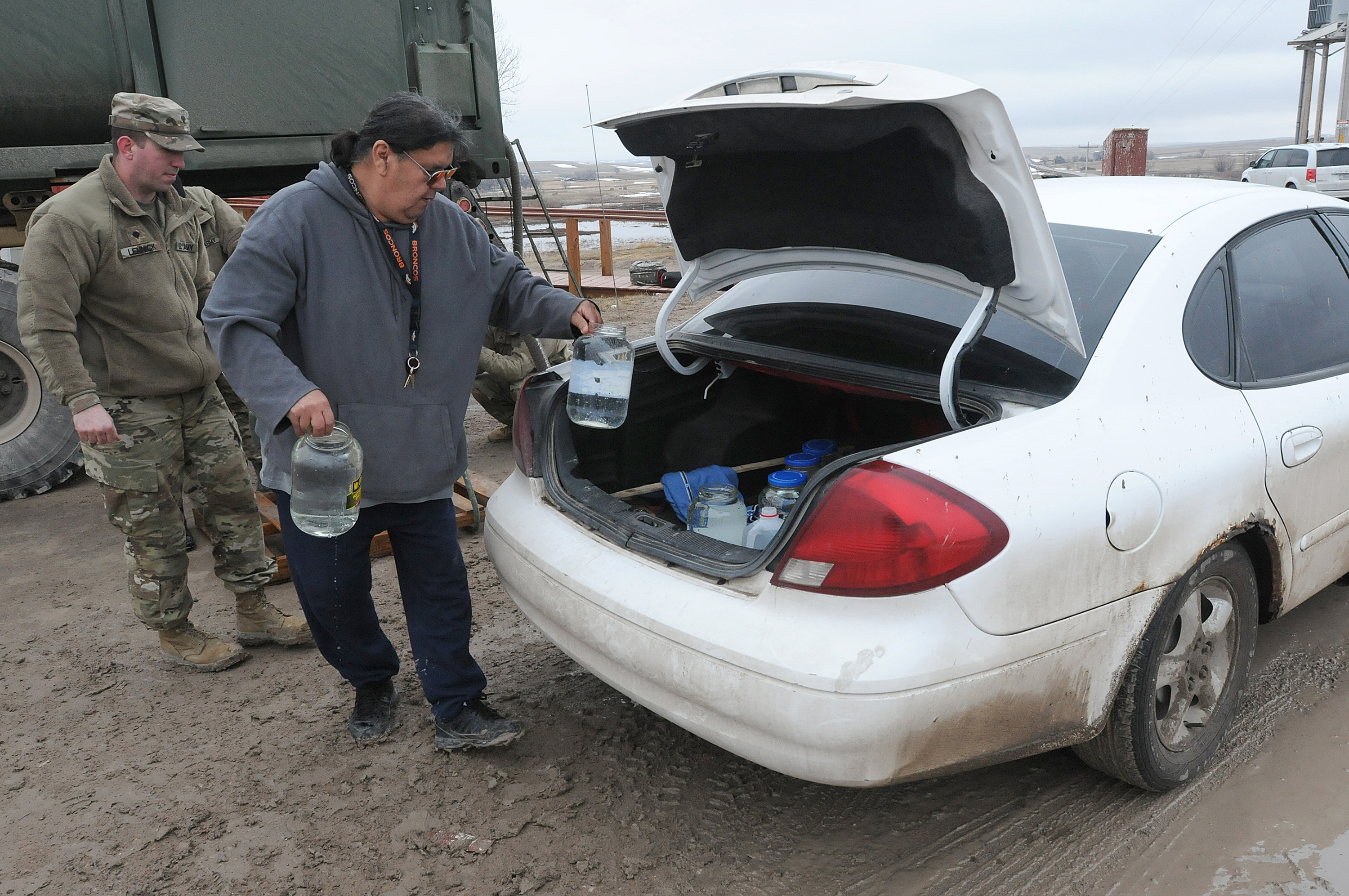 A man loads jugs of water into the trunk of his car.