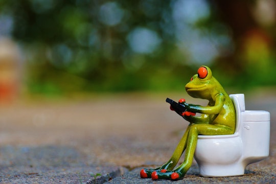 A ceramic frog holding a phone sitting on a tiny toilet.