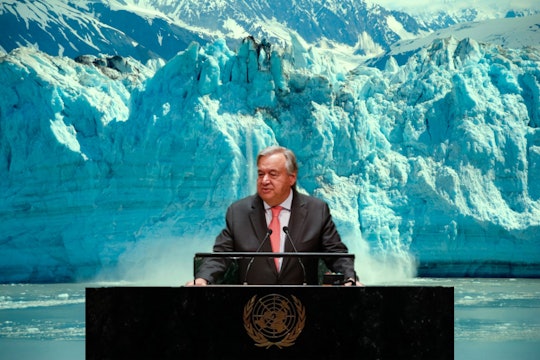 Guterres Iceberg Antonio Guterres stands at a desk in front of a calving glacier