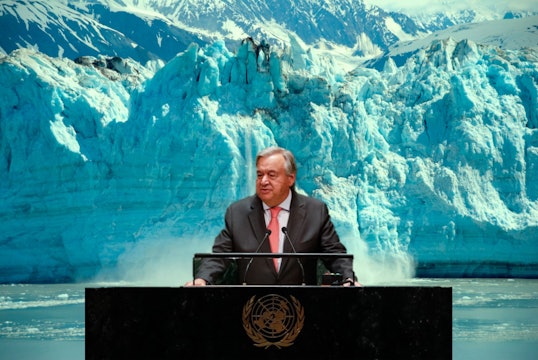 Antonio Guterres stands at a desk in front of a calving glacier