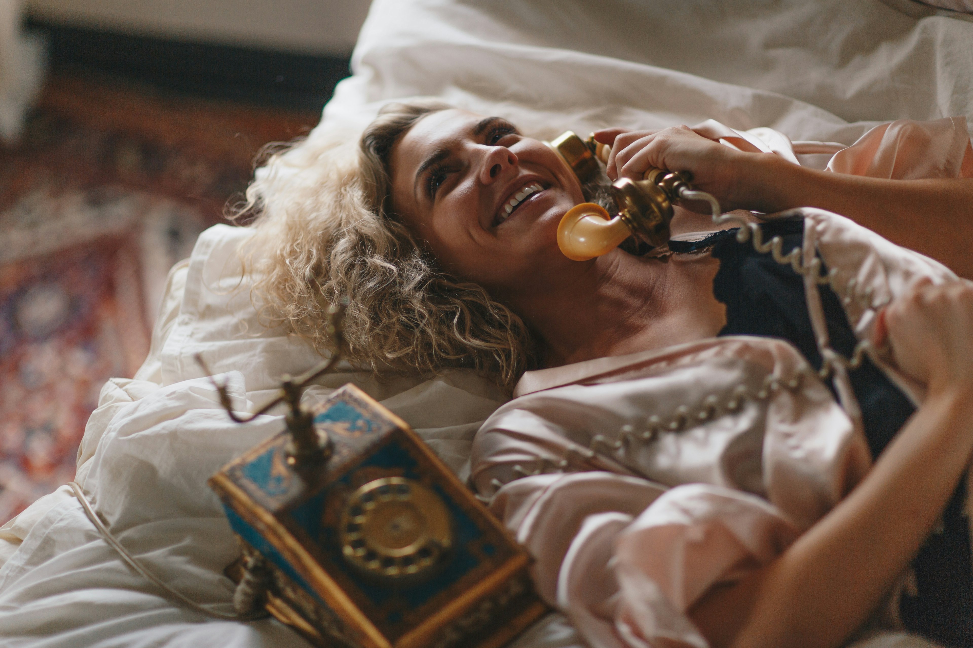 A woman laying on a bed talking on an old-timey rotary phone.