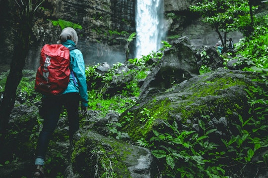 a woman wearing a hijab with a red backpack hiking to a waterfall