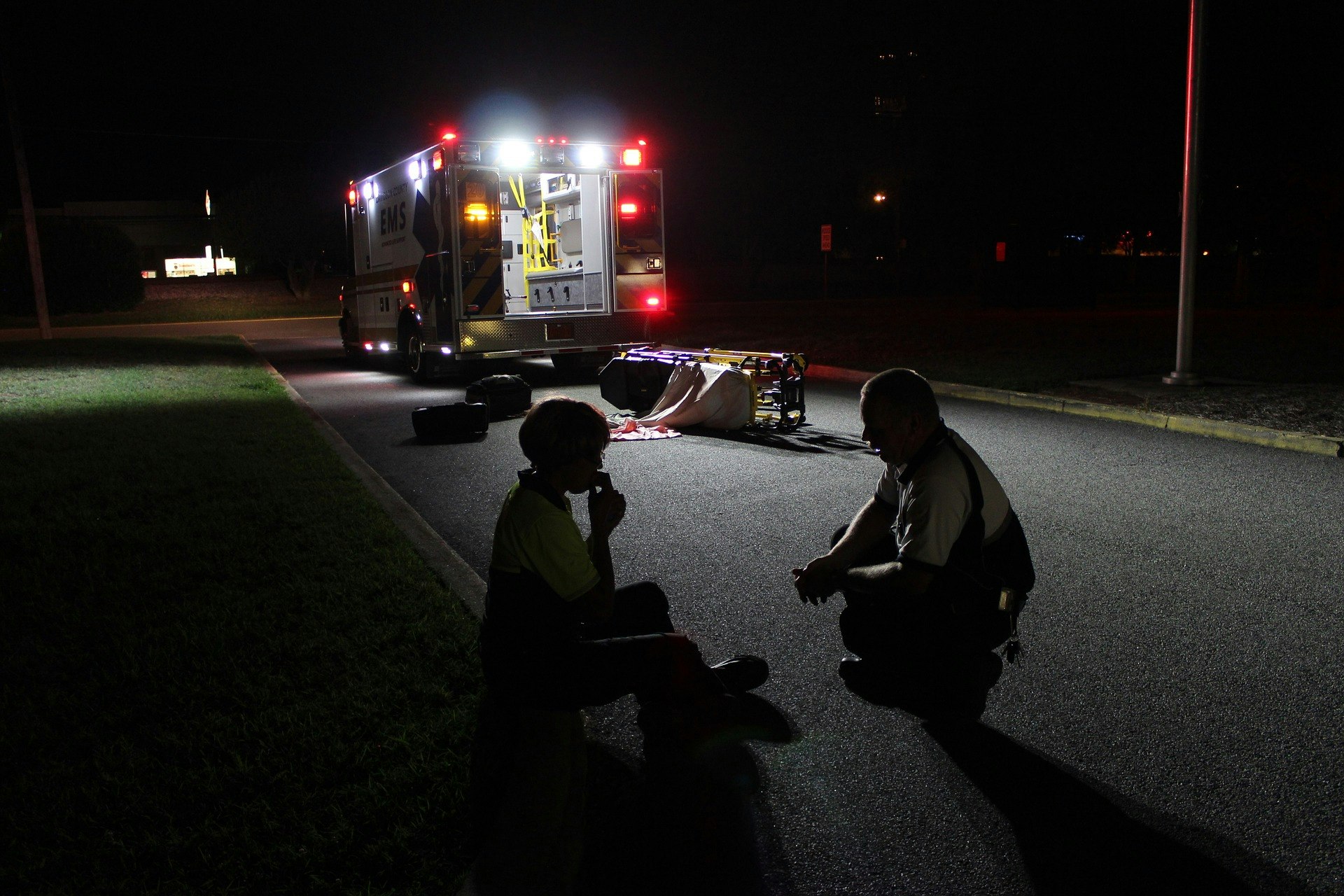 A paramedic talks to a patient on a darkened street next to an ambulance with its lights flashing.
