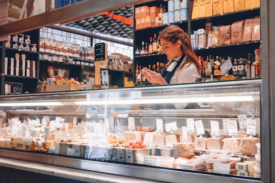 A clerk stands behind the counter of a deli stocked with meat and cheese.