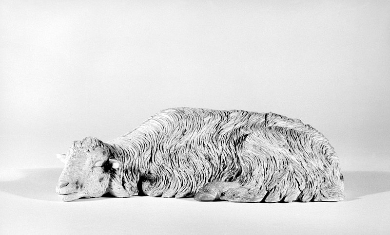 A metal and ceramic sculpture of a sleeping sheep on a white background.