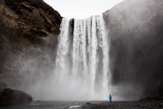 waterfall and person a person standing at the bottom of a huge waterfall