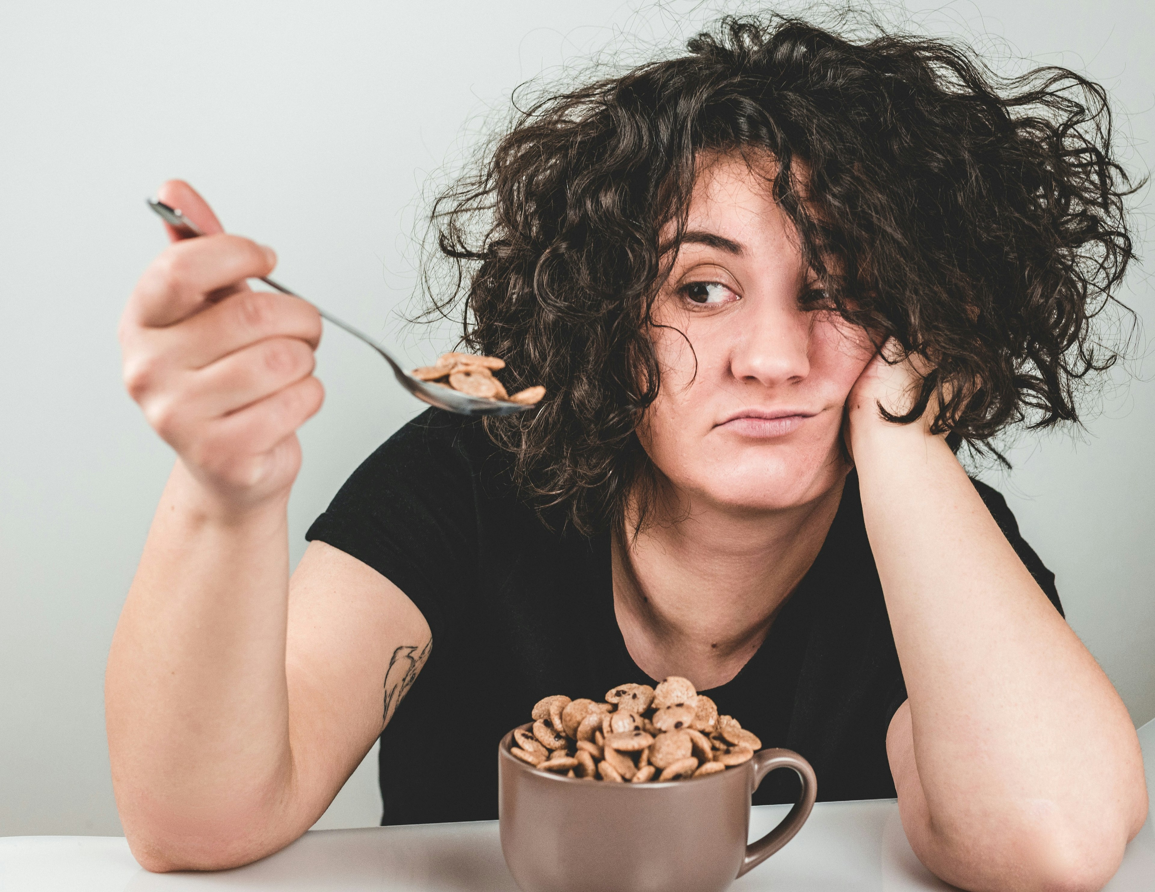 a stressed-looking woman eating from a mug of cereal