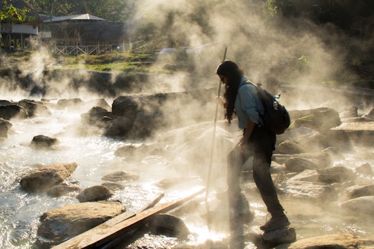 a woman with long hair leans over a river with mist