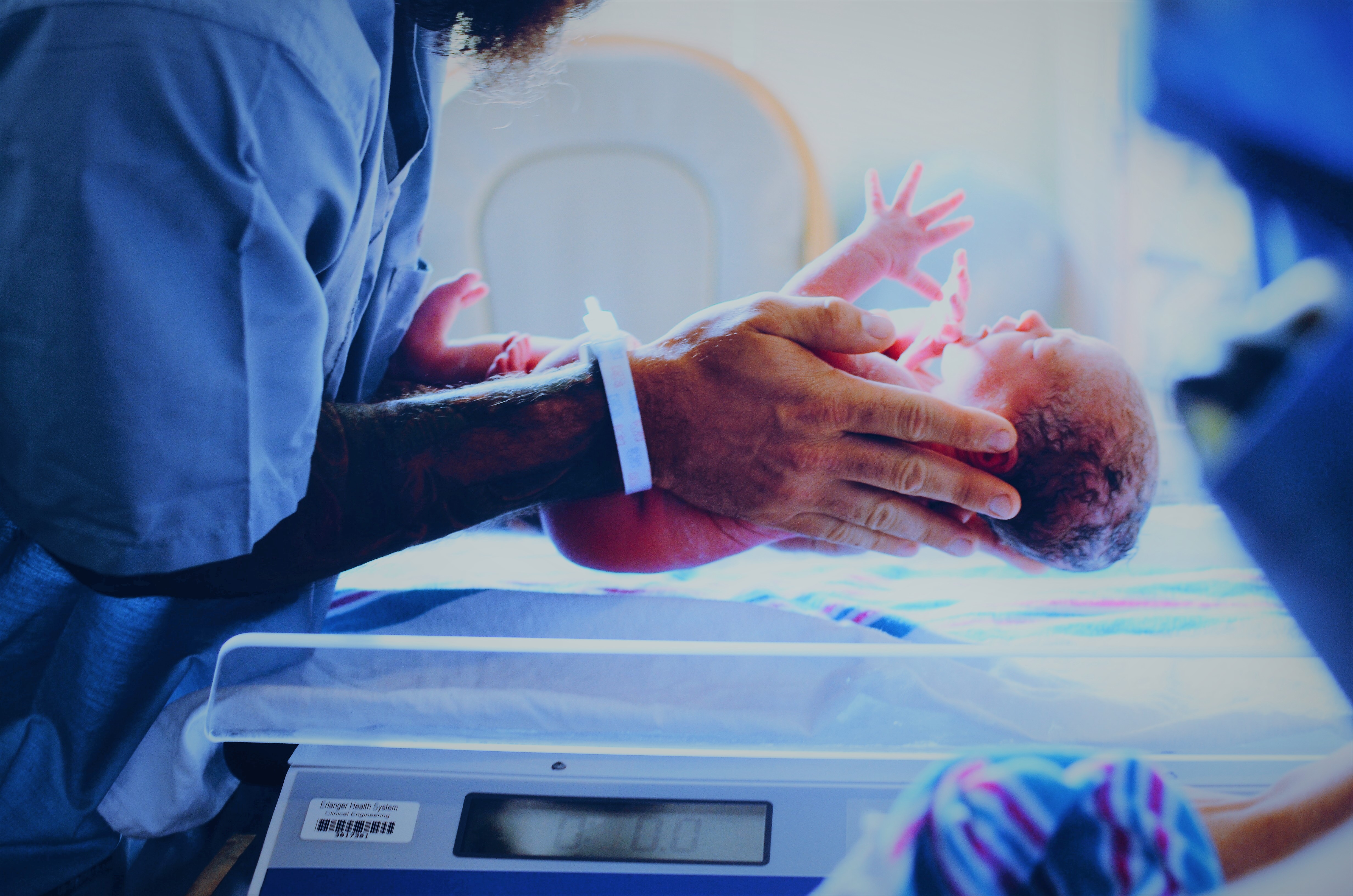 Newborn baby help by person in a hospital gown being weighed on a scale