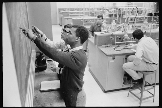 Two students point at a chalkboard in a chemistry lab