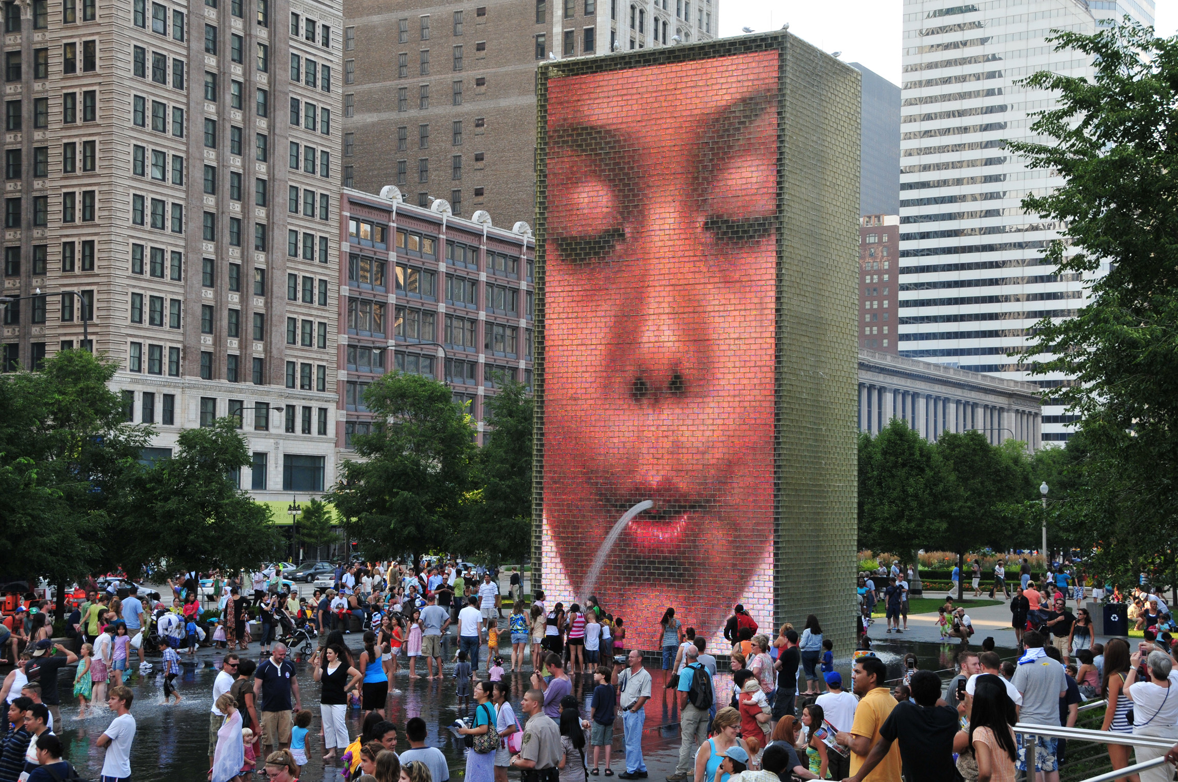A crowd gathers around Crown Fountain in Chicago's Millenium Park, where a fountain appears to "spit" water on visitors.