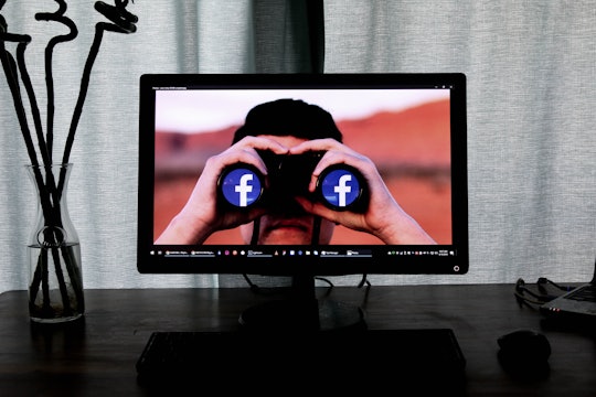 a computer screen background showing a person peering through binoculars with the facebook logo on the ends of them