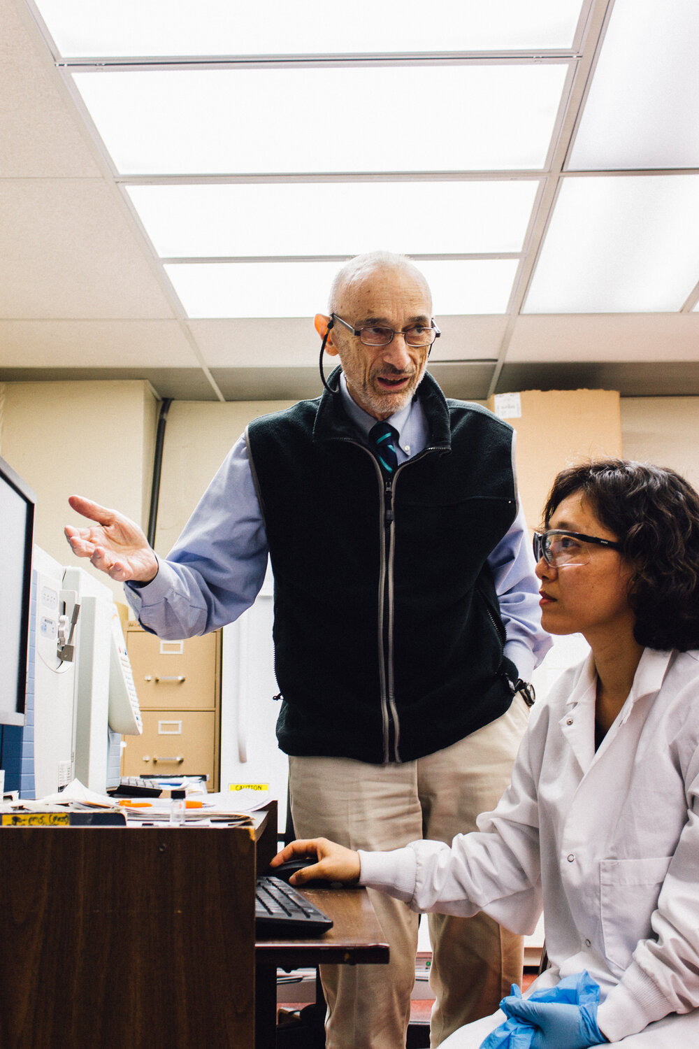 Two scientists in a lab, one standing and gesturing with an han