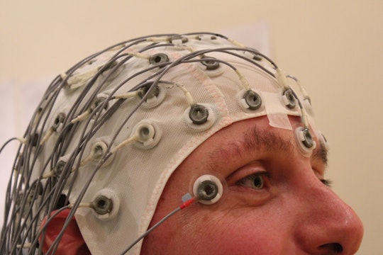A man wearing an electroencephalography cap, with many wires protruding from a white nylon hat.