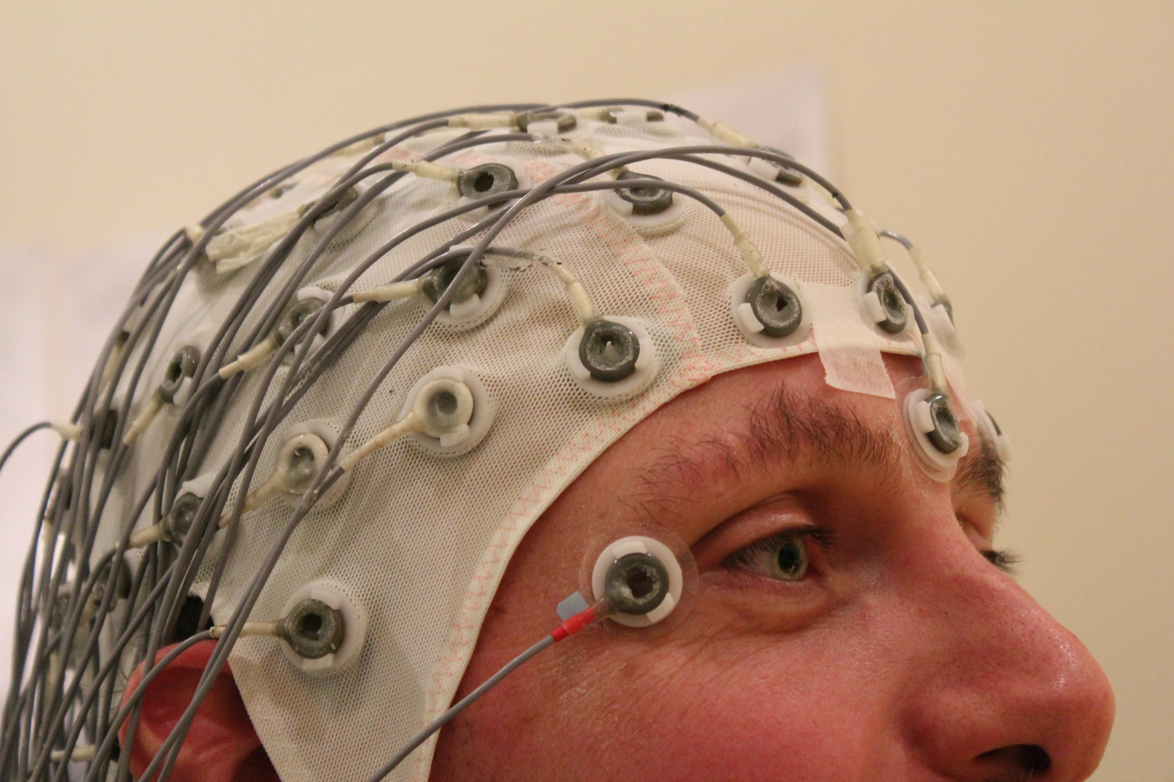A man wearing an electroencephalography cap, with many wires protruding from a white nylon hat. 