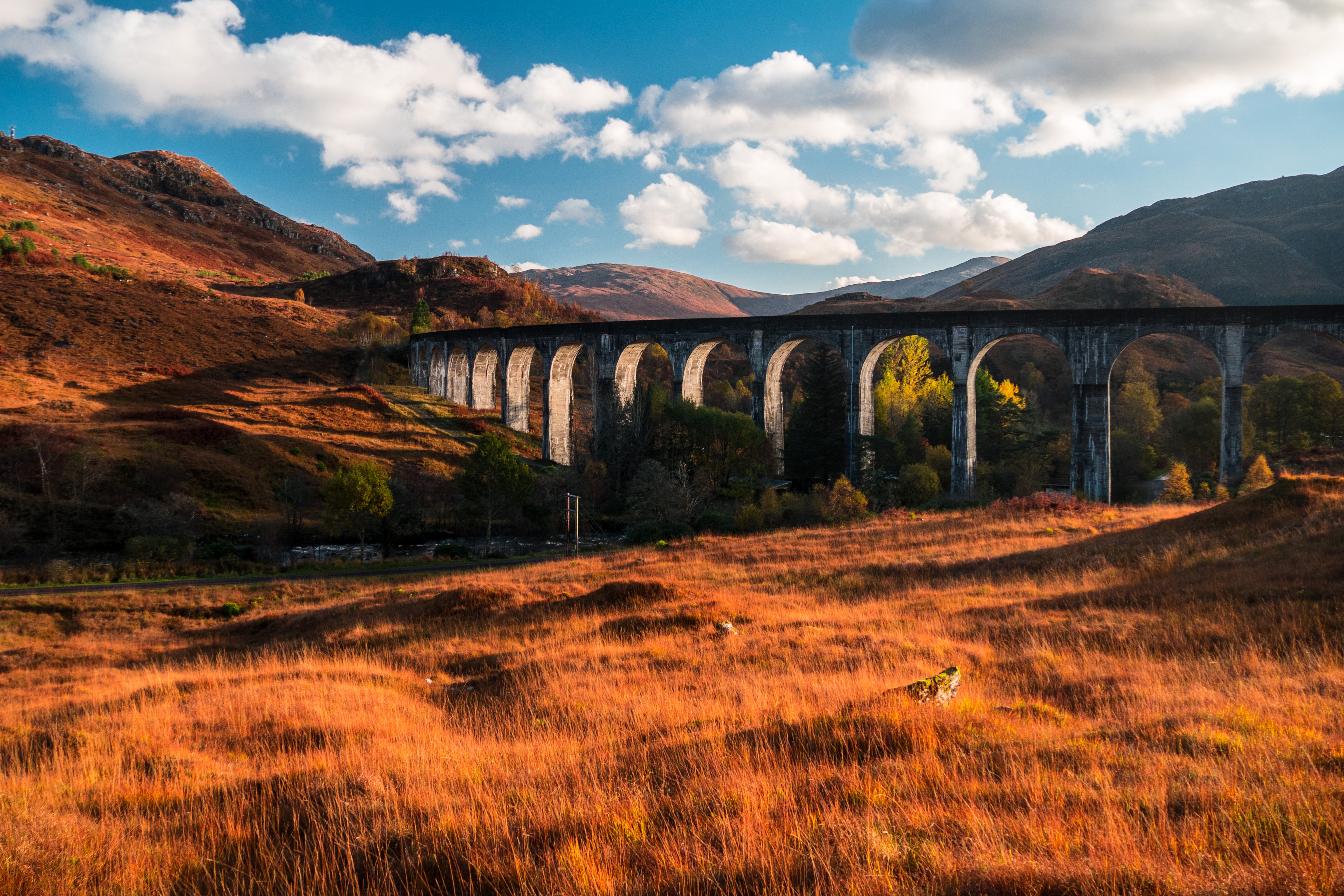 a bridge with a field in front and a bright blue sky behind it