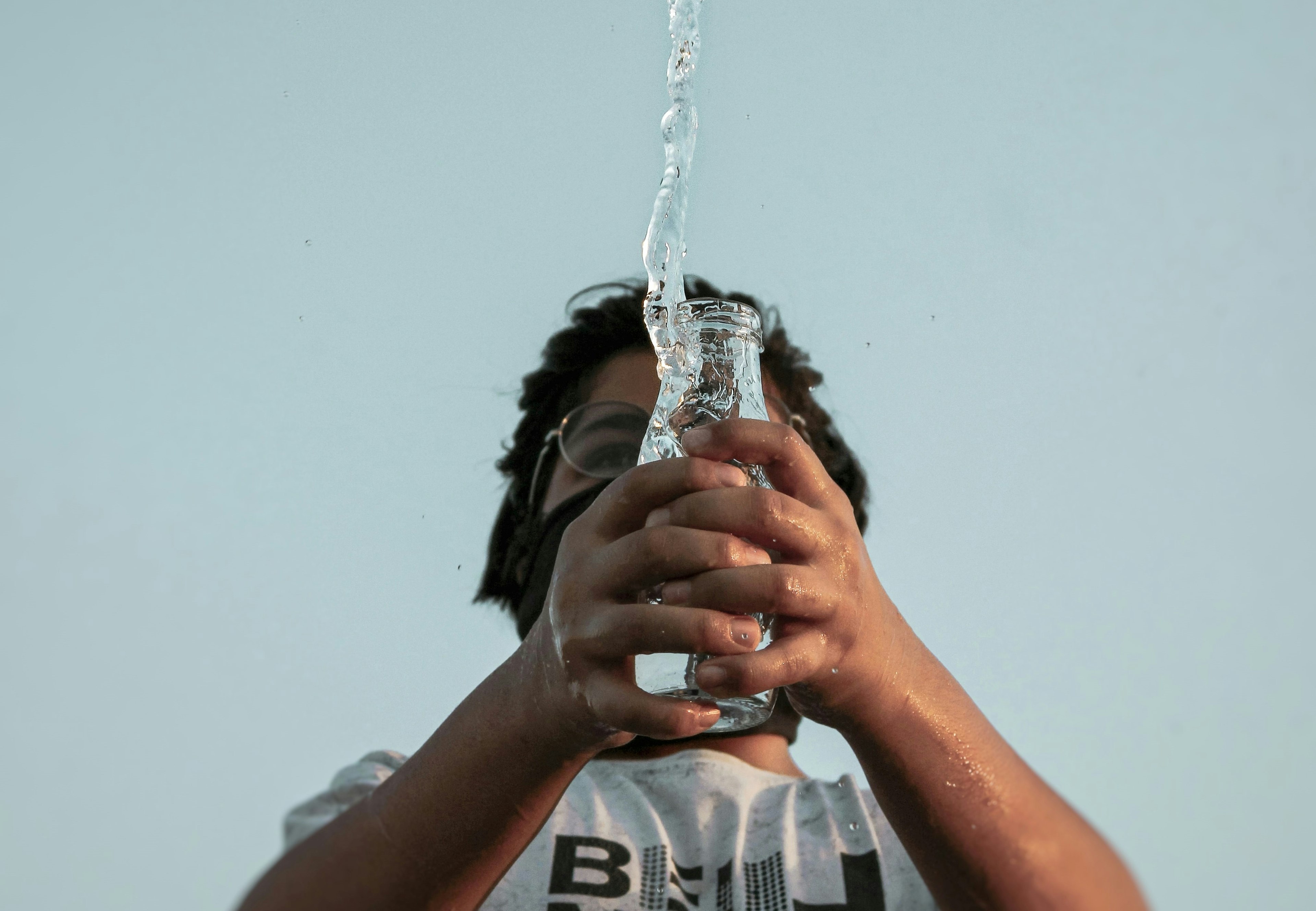 a man spilling water out of a glass jar, photographed from below