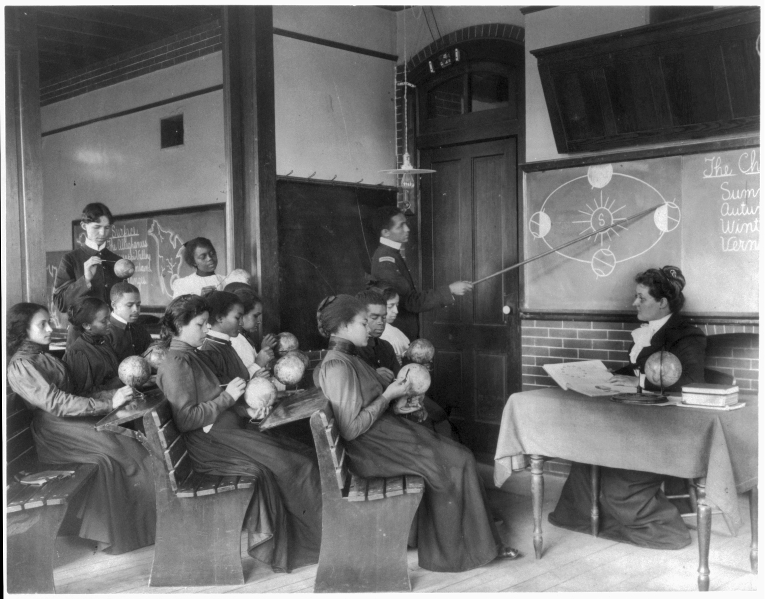 A black and white photo of school students holding small globes learning about the Earth's rotation around the Sun in 1899
